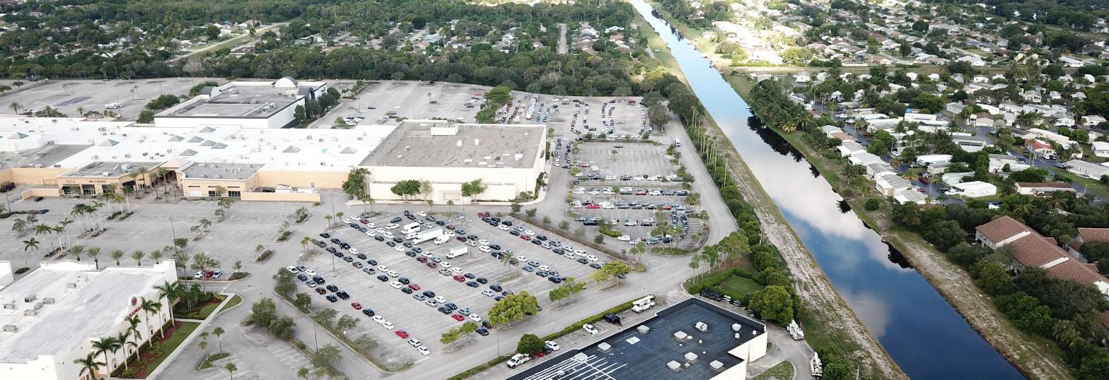 High-altitude aerial view of a Palm Beach County shopping plaza beside a canal, at golden hour