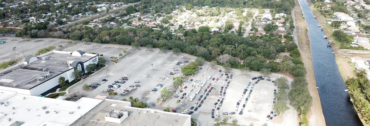 Aerial view of a parking lot bordered by tree canopy and a canal